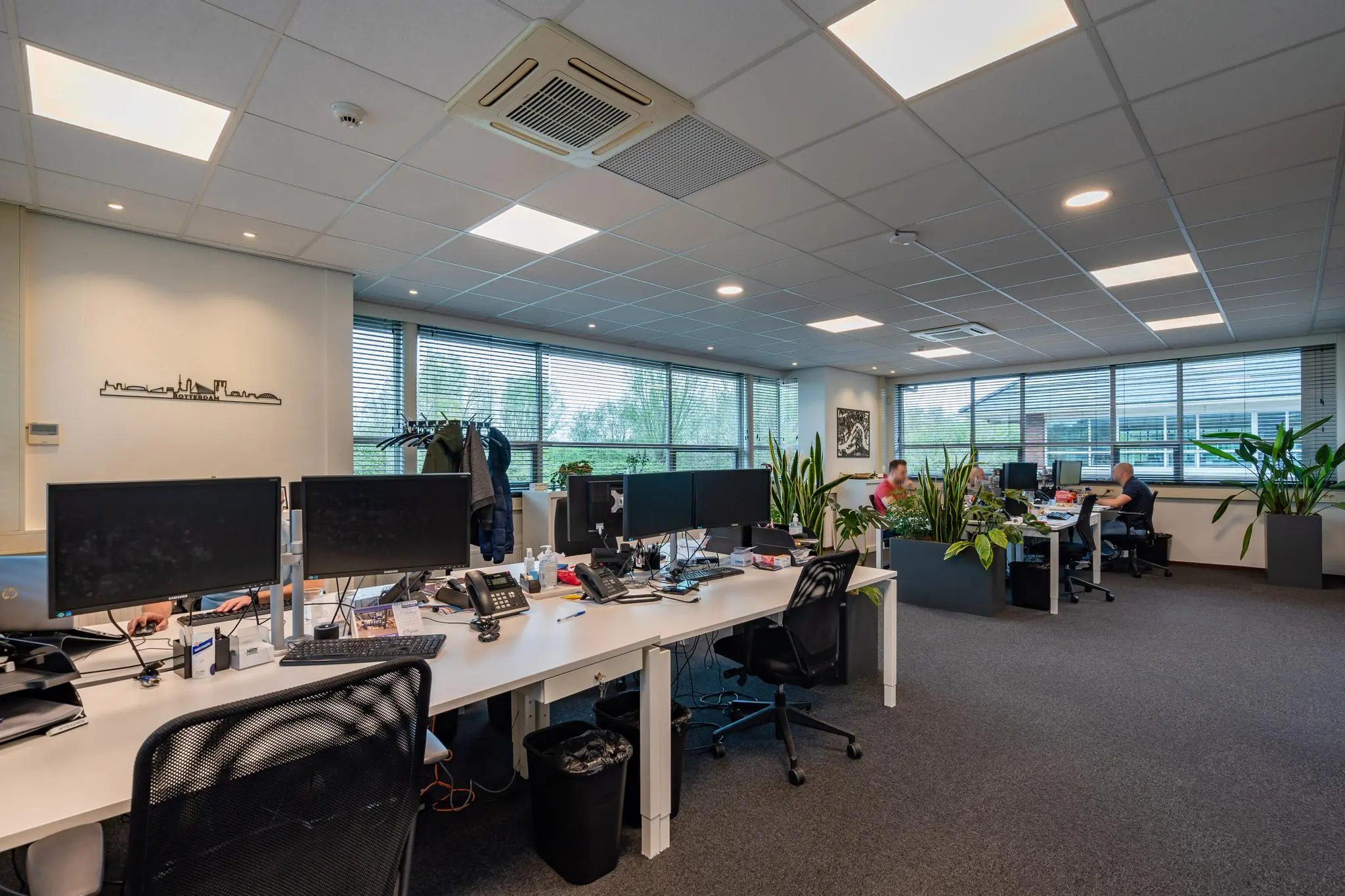 Modern kantoorinterieur aan de 1e Barendrechtseweg met werkplekken, computers en veel kamerplanten.